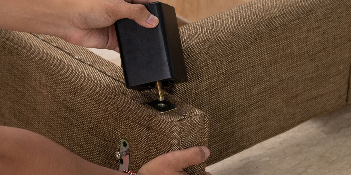 Pengrajin memasang kaki kayu solid pada rangka divan berlapis kain